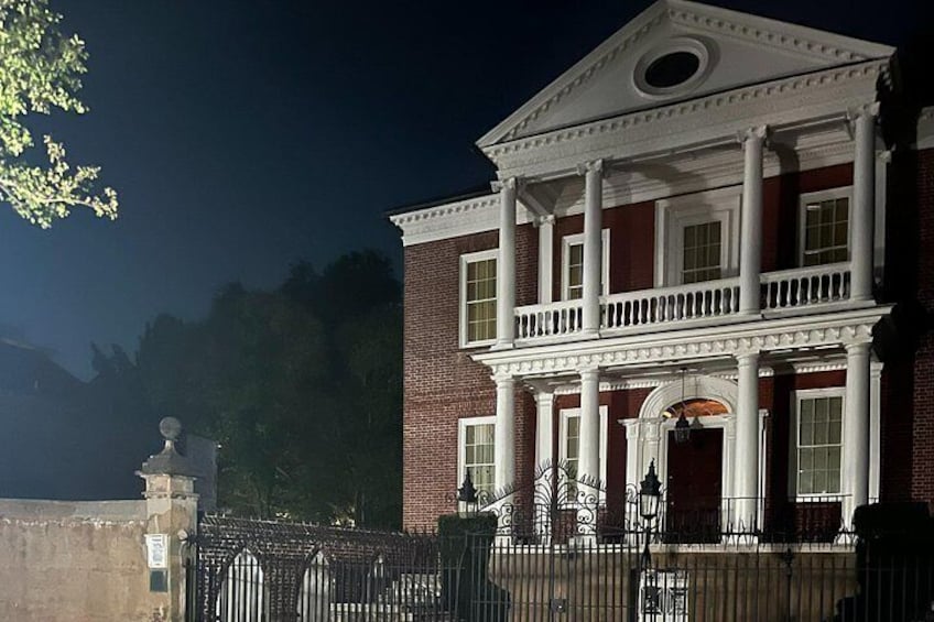 A large brick building with white columns and a balcony, surrounded by a metal fence. 4