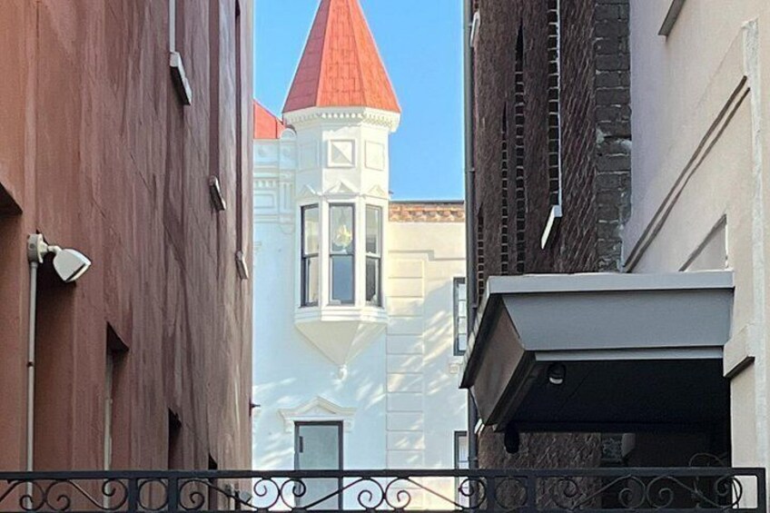 A narrow street with a red-roofed tower and a white building with a bay window. 2