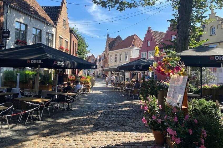 A cobblestone street with outdoor cafes, flower arrangements, and traditional European buildings. 1