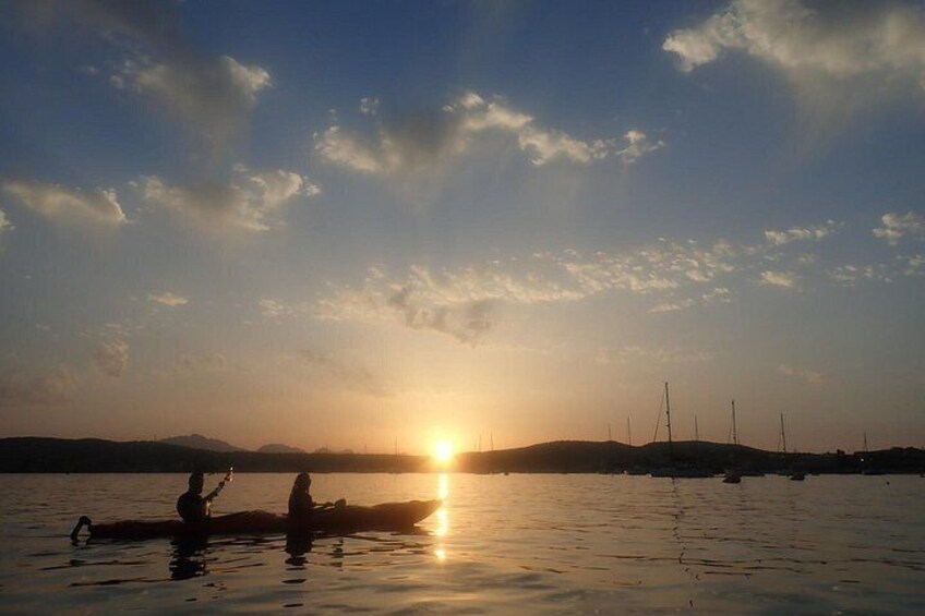 A sunset over a calm body of water with silhouettes of people and boats. 2