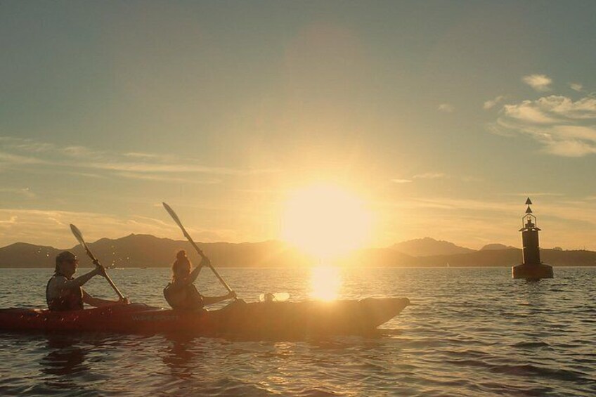 Two people kayaking on a calm body of water during sunset with a lighthouse in the background. 1