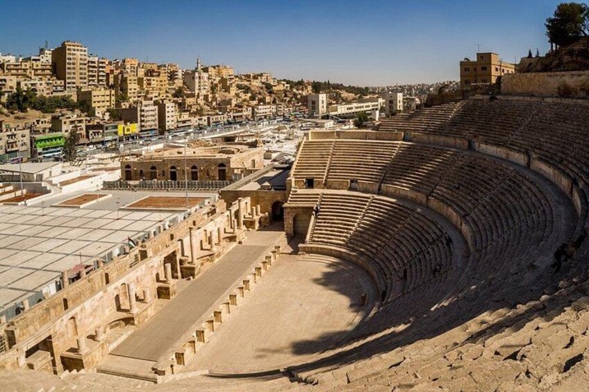 Un antiguo anfiteatro con asientos escalonados, rodeado de edificios históricos y un cielo despejado. 2