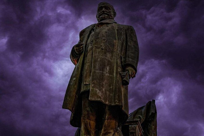 A statue of a person wearing a long coat and hat, set against a cloudy sky. 2