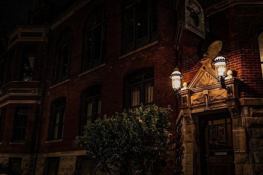 A brick building with ornate architectural details and two lit street lamps. 5