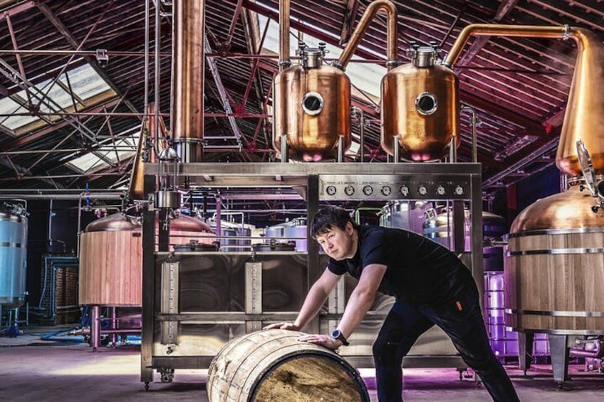 A person working with a large barrel in a brewery with copper tanks and industrial equipment. 3