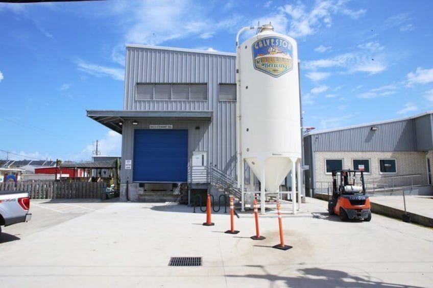 A large industrial building with a blue garage door, a white silo, and a forklift parked in front. 2