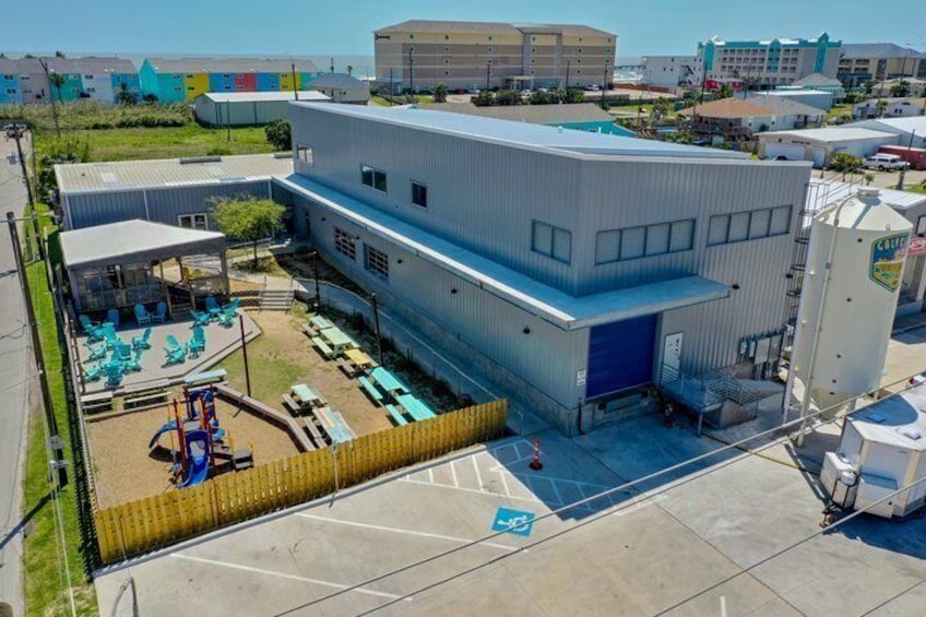 A large industrial building with a blue garage door, a fenced playground, and a parking lot. 5