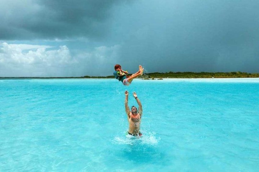 Una persona nada en un océano azul y transparente, mientras un niño es levantado por encima del agua. 2