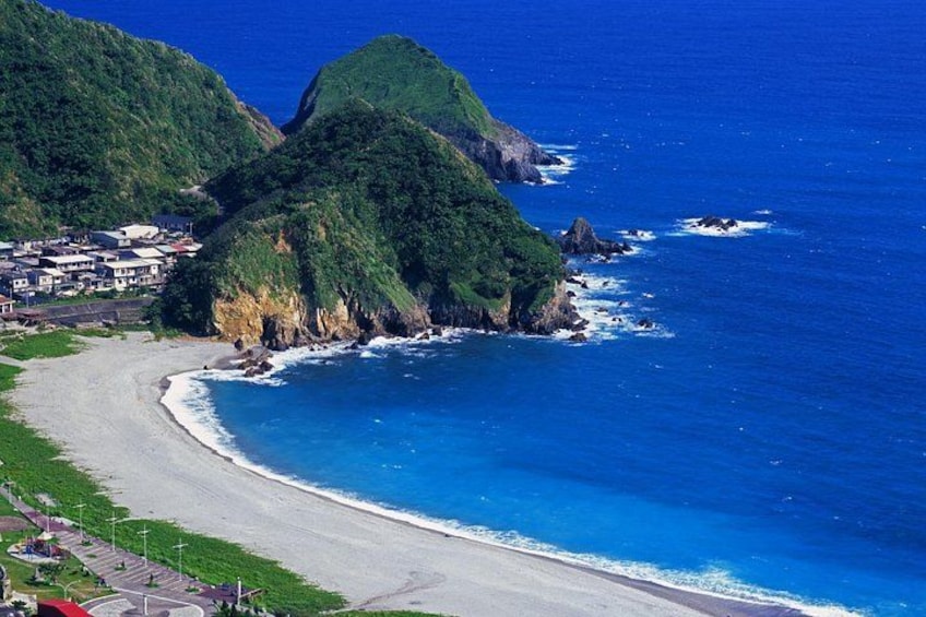 A coastal landscape with a beach, a small settlement, and green hills. 4
