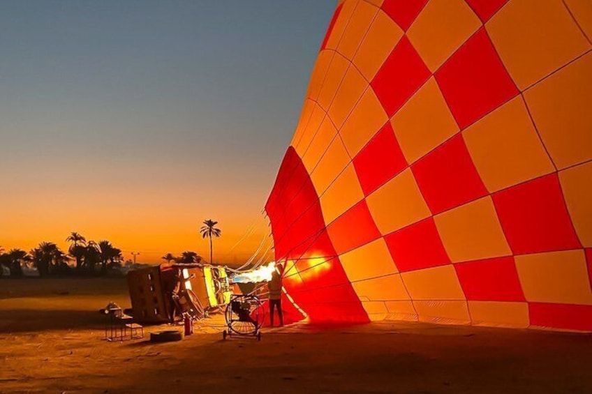 En varmluftsballon med ternet mønster, parkeret på jordbund med palmer i baggrunden. 3