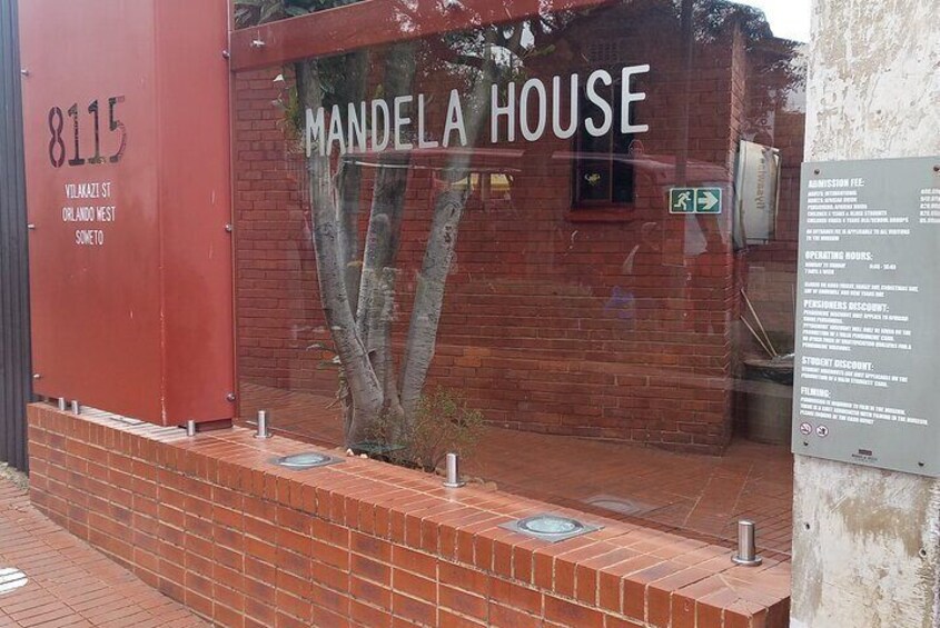The exterior of Mandela House, including the address 8115 Vilakazi St, Orlando West, Soweto, and a sign detailing admission fees and operating hours. 1