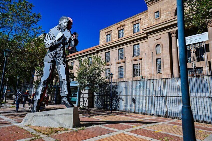 A statue of a man in a suit, a building with arched windows, and a paved plaza with a fence. 3