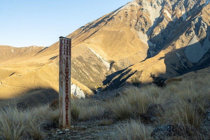 A weathered signpost in a grassy field with mountains in the background. 5