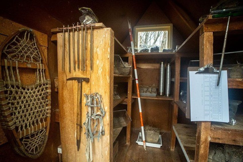 A rustic wooden structure with tools, a ladder, and a metal container. 3
