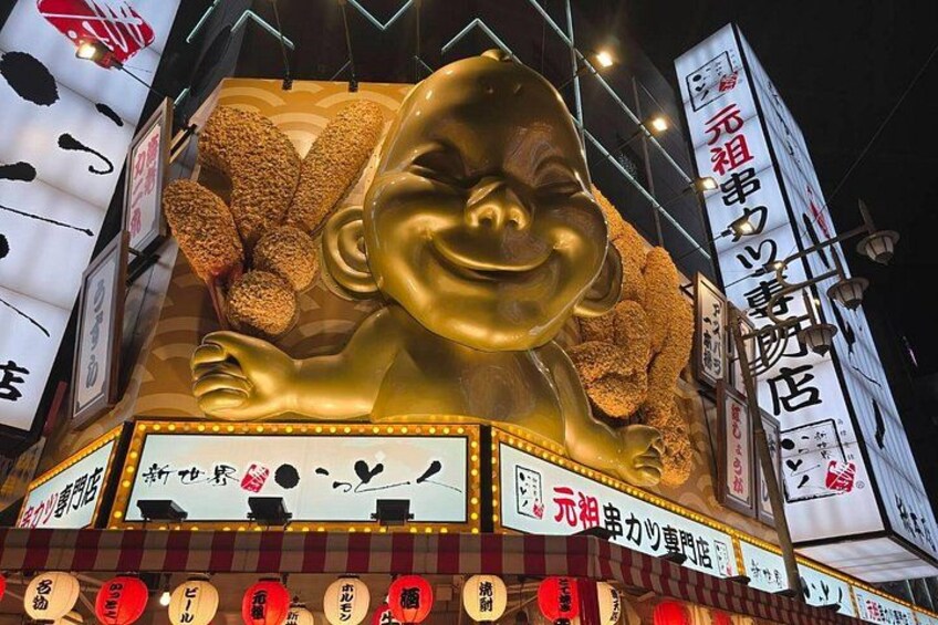 A large golden statue of a smiling face with hands raised, surrounded by illuminated signs and traditional Japanese decorations. 5