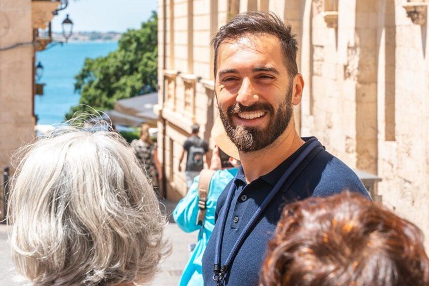 A man in a blue shirt walking on a street with buildings and a body of water in the background. 3