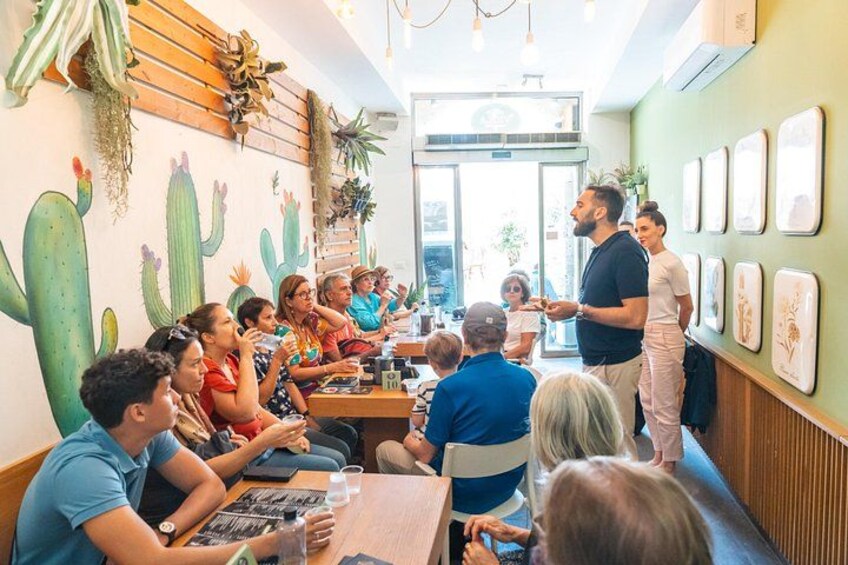 A group of people seated at tables in a room with cactus wall art and framed pictures. 4