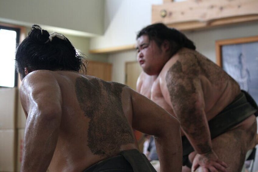 Two sumo wrestlers in a room with a painting on the wall. 4