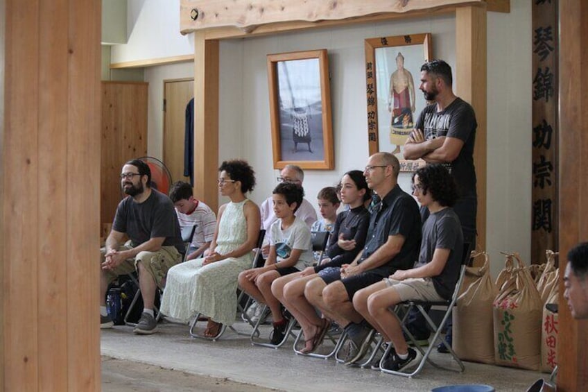 A group of people sitting in chairs outdoors, some with bags beside them. 3