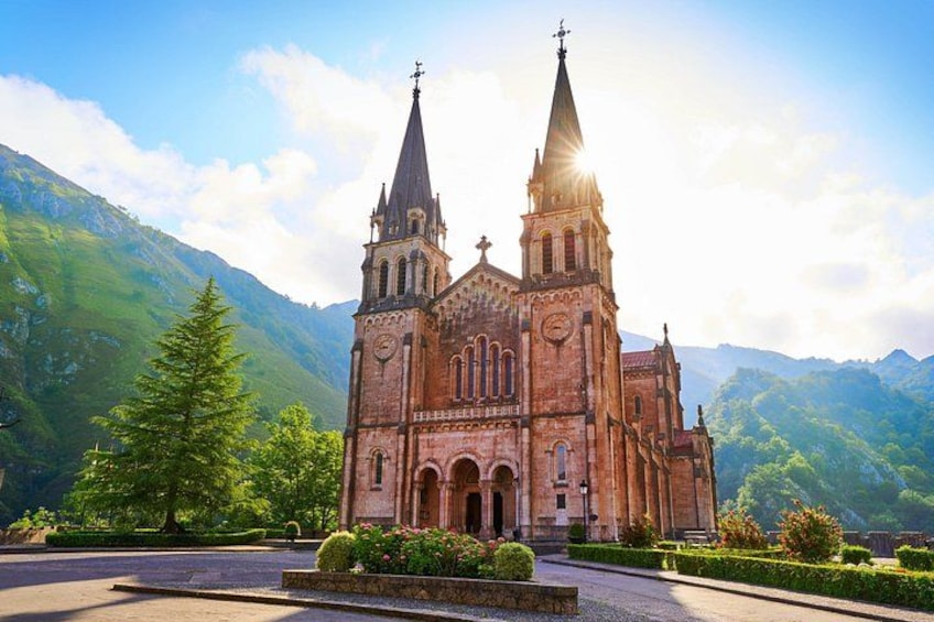 A large brick church with two tall spires, surrounded by lush green mountains and a clear sky. 4