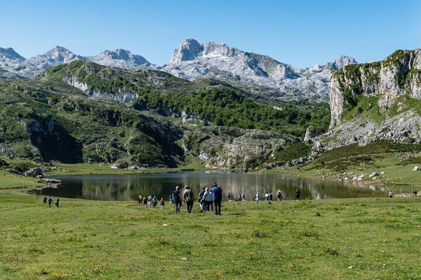 A lake surrounded by mountains, a grassy area with people walking, and rocky cliffs. 1