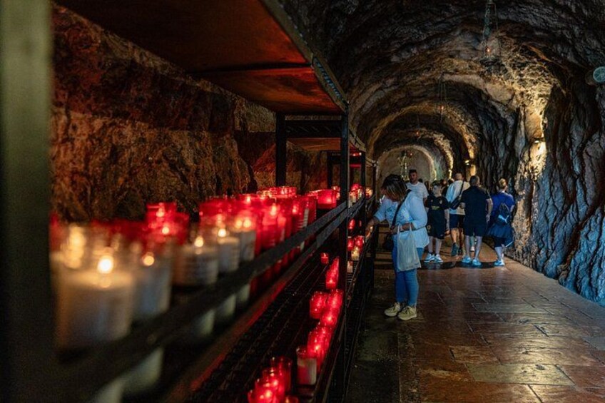 A tunnel with stone walls, red candles, and people walking. 2