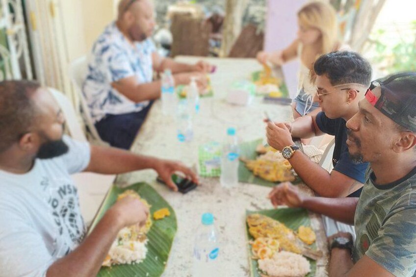 A group of people sitting around a table with food on banana leaves. 3