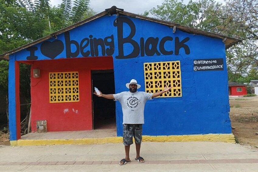 A person standing in front of a colorful building with the words 'I love being Black' painted on it. 1
