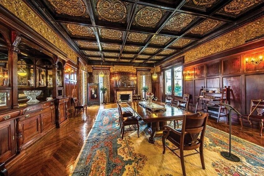 An ornate room with a long wooden table, chairs, and a patterned carpet. 1