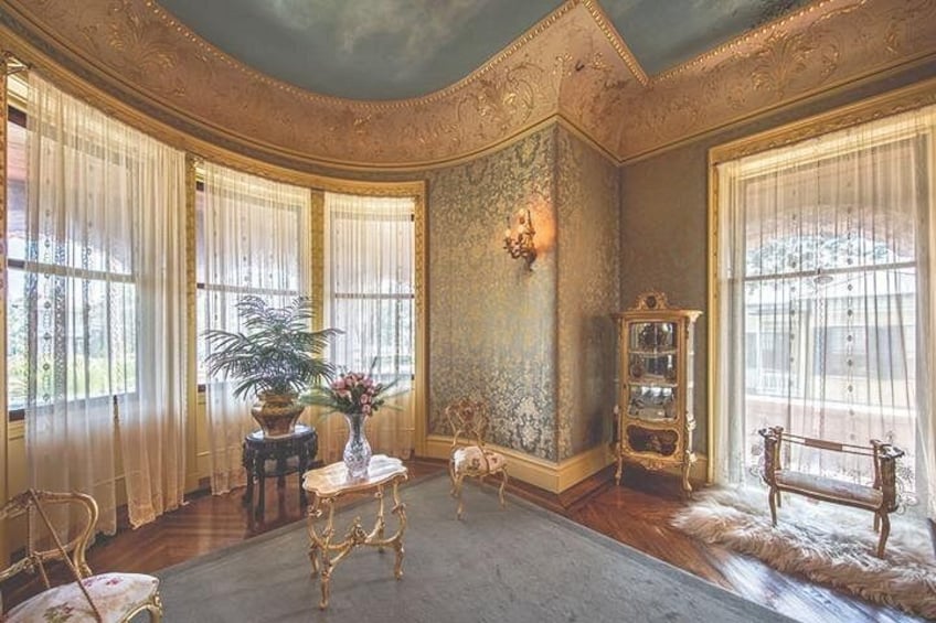 Una sala imponente con muebles ornamentales, un jarrón grande con flores y un globo terráqueo sobre un atril. 2