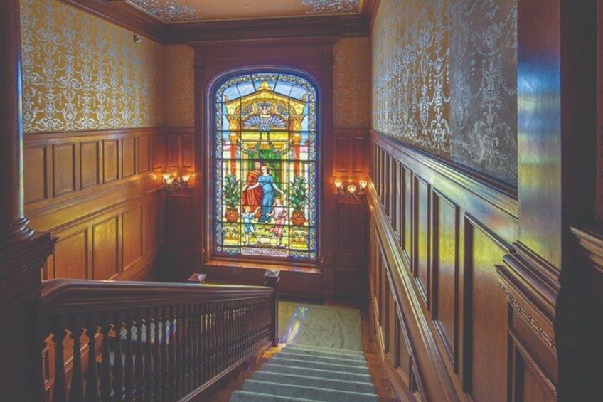 Una gran escalera con paneles de madera decorativos y un ventanal de vidrio emplomado en la parte superior. 5