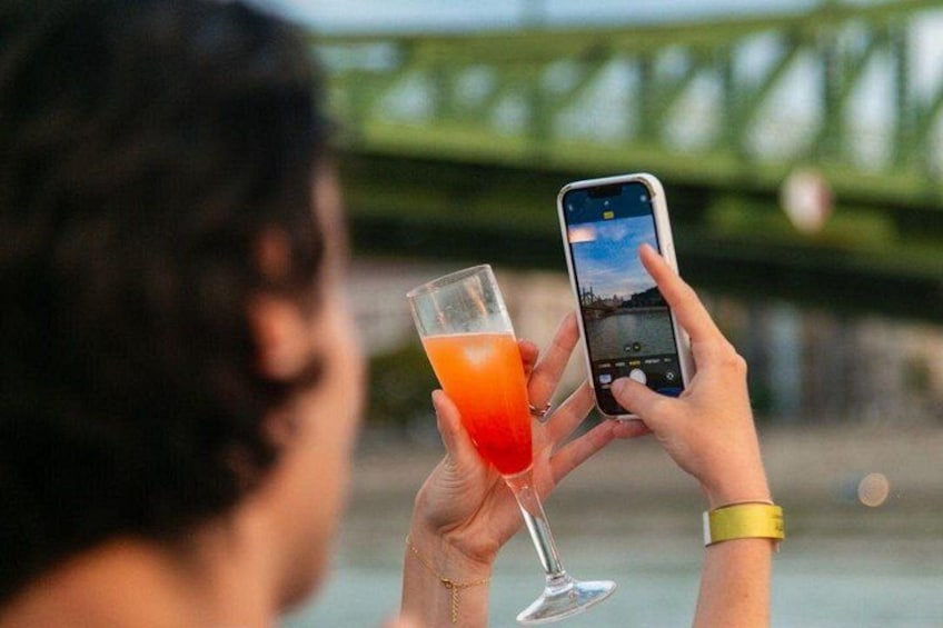 Iemand houdt een glas sinaasappelkleurig vocht vast en maakt een foto met een smartphone. 3