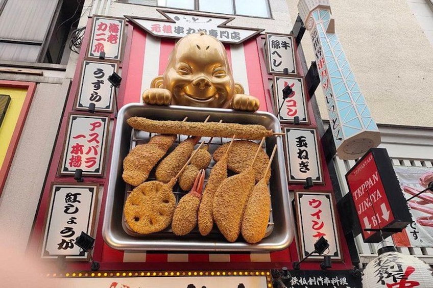 A food stall with various fried items displayed on a tray, surrounded by Japanese signage. 2