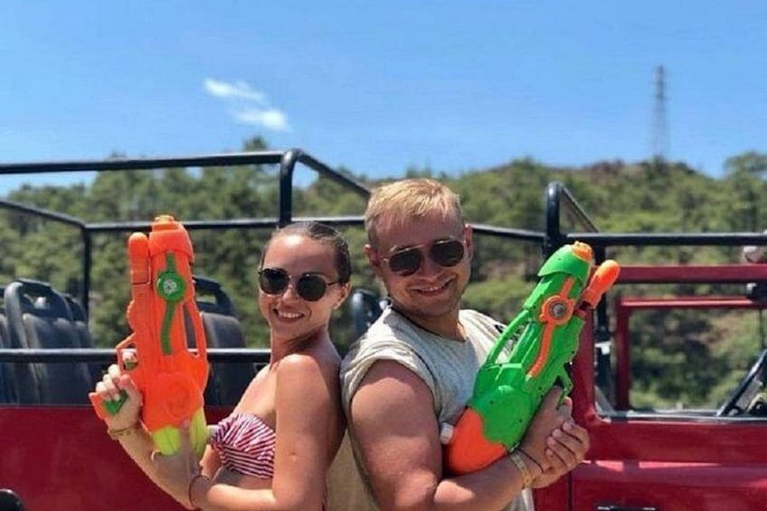 Two people holding toy guns, a red vehicle, and a natural landscape with trees in the background. 4