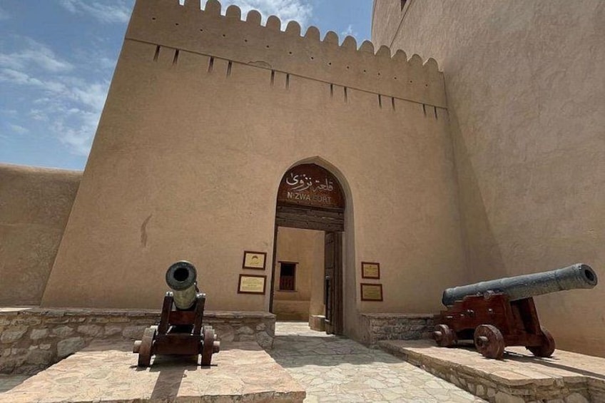 A historical building with a large arched entrance, two cannons, and a stone pathway. 1