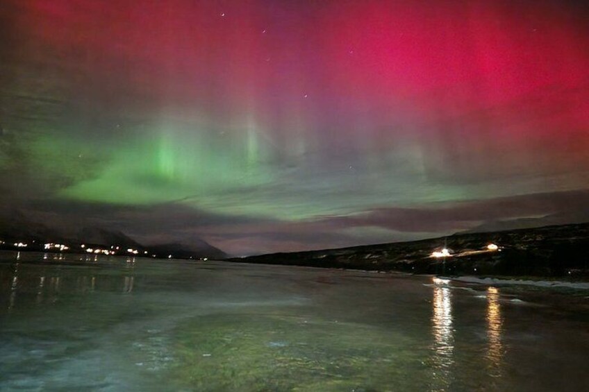 Escena nocturna con auroras boreales sobre un paisaje helado, con luces a lo lejos. 2