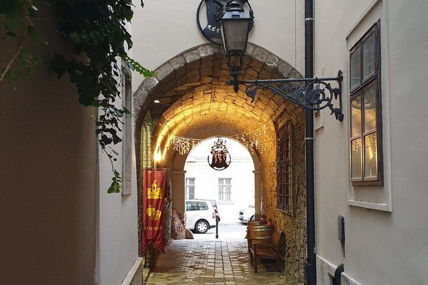 Une ruelle étroite avec une arche en briques, un luminaire suspendu et un tonneau en bois. 5