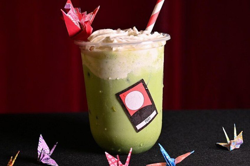 A green beverage with a straw and whipped cream, a red and white label, and origami decorations. 3