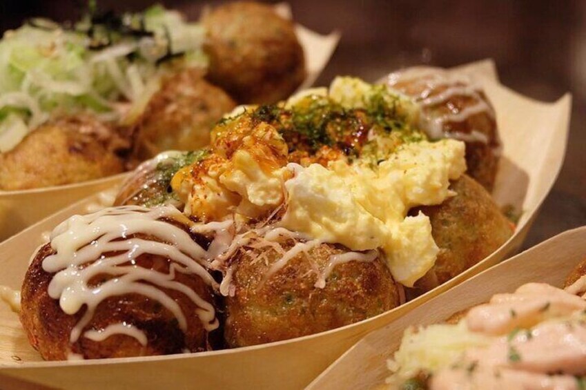 A variety of fried food items, including breaded balls with different toppings such as mayonnaise, green herbs, and a white sauce. 1