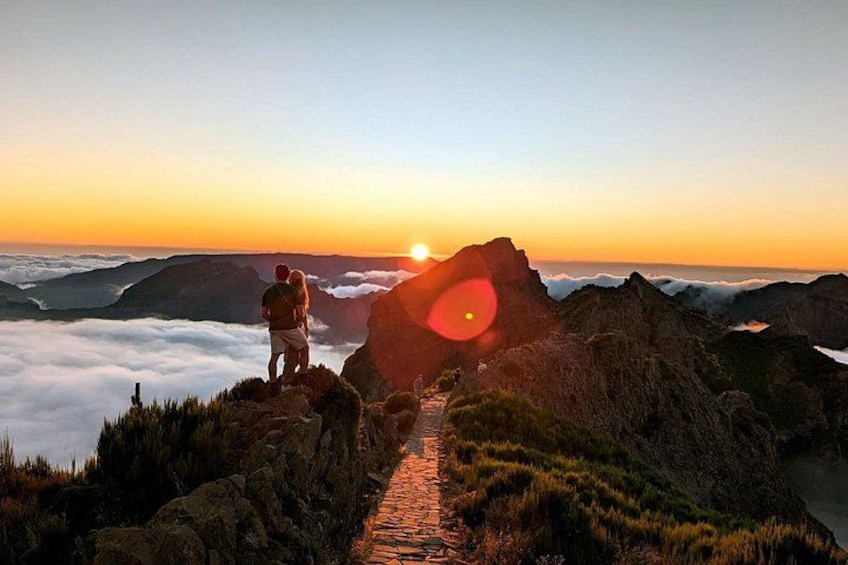 A person standing on a rocky outcrop overlooking a valley with a sunrise in the background. 4