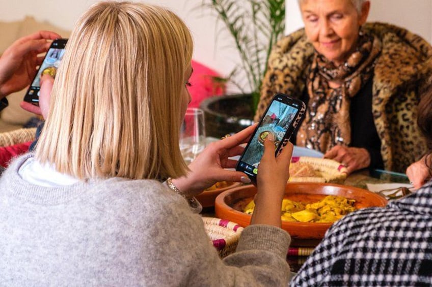 Une personne tenant un smartphone, une autre personne dont le visage est flou, et une table avec de la nourriture. 3