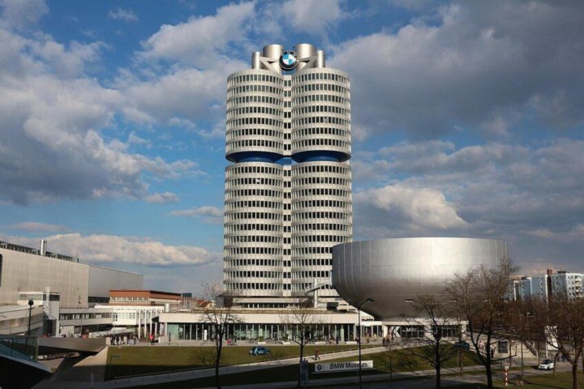 Un edificio alto y cilíndrico con el logo de BMW, rodeado de un área verde y otros edificios. 4