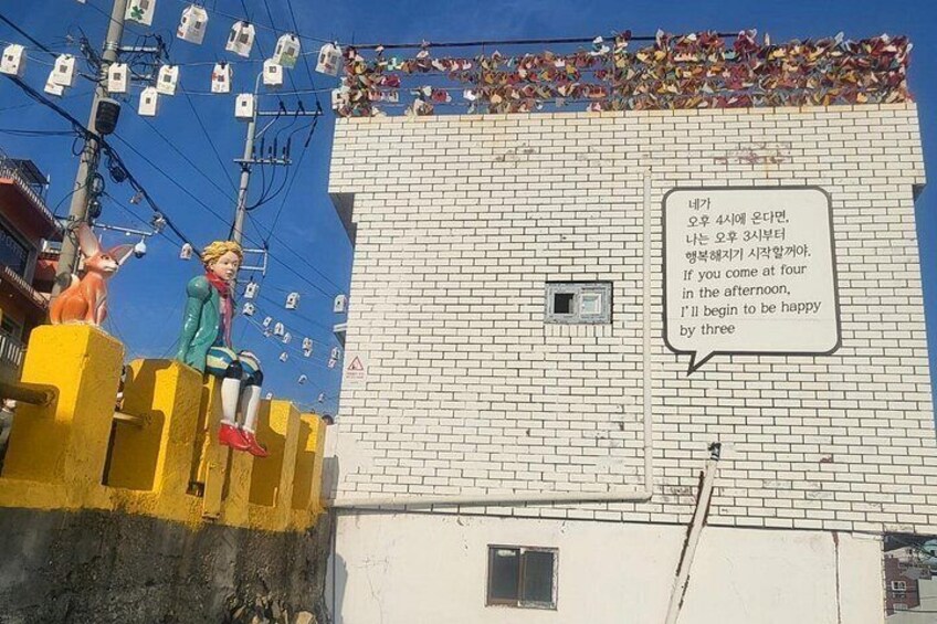 Un edificio con fachada de ladrillo, cerca amarilla y un bocadillo de diálogo con texto coreano. 1