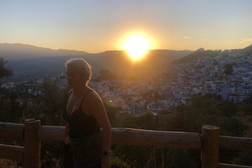 Une personne se tient sur une colline, d’où elle a une vue panoramique sur la ville, avec le soleil couchant à l’horizon. 3