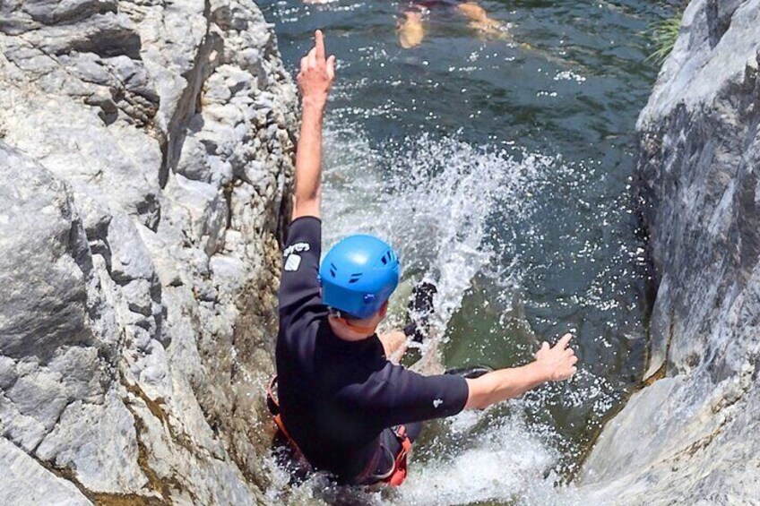 A person in a wetsuit and helmet jumping into a rocky water body. 5