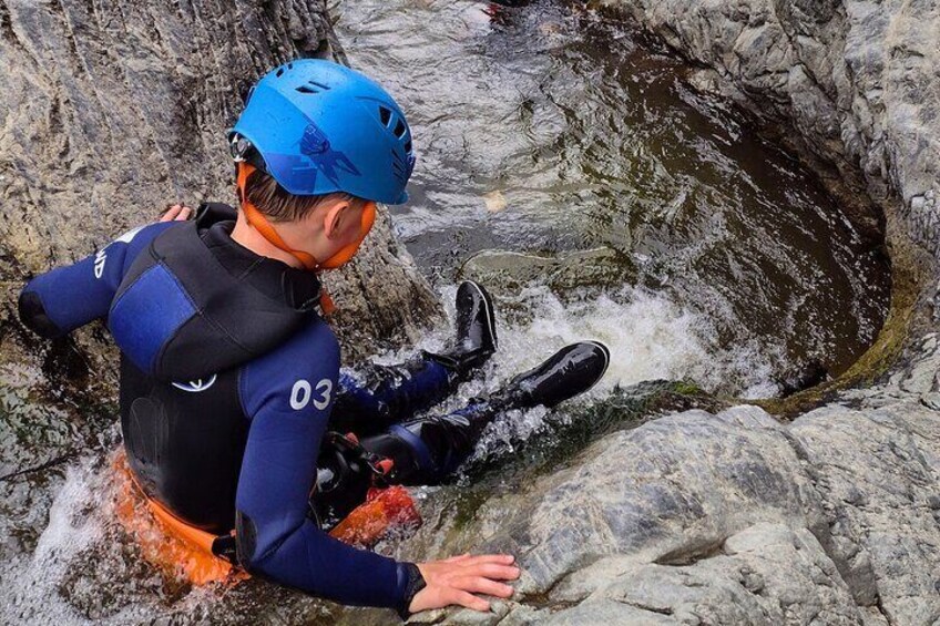A person in a wetsuit and helmet sitting on a rock by a flowing river. 3