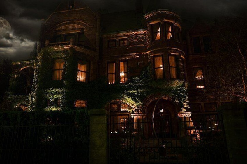 A large, historic house with ivy-covered walls and multiple windows lit from the inside. 2
