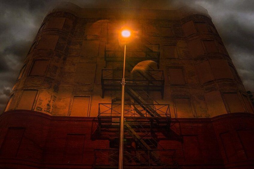 A tall, cylindrical industrial building with a staircase leading to a platform, under a cloudy sky. 2
