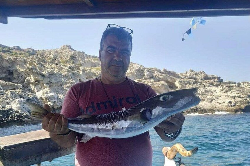 En person holder en stor fisk, med klippefyldte kyster og havet i baggrunden. 1