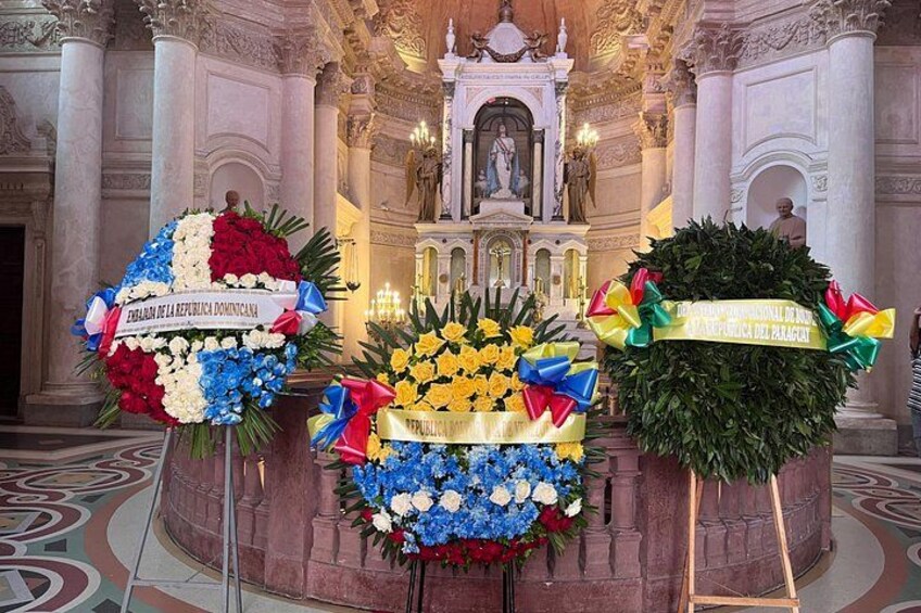A ceremonial hall with floral tributes, a statue, and ornate architecture. 4